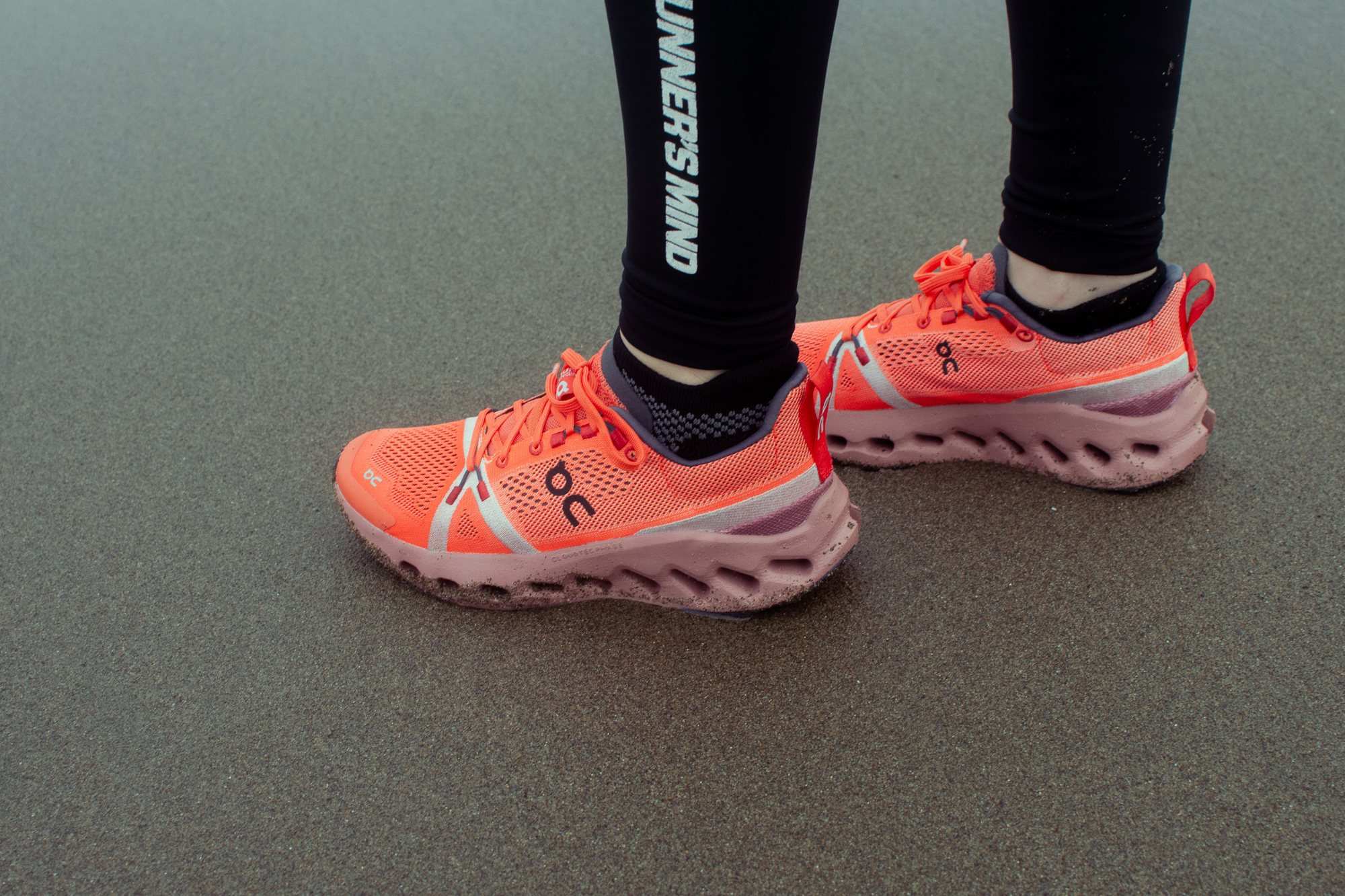 A person's legs and bright orange running shoes on a grey floor