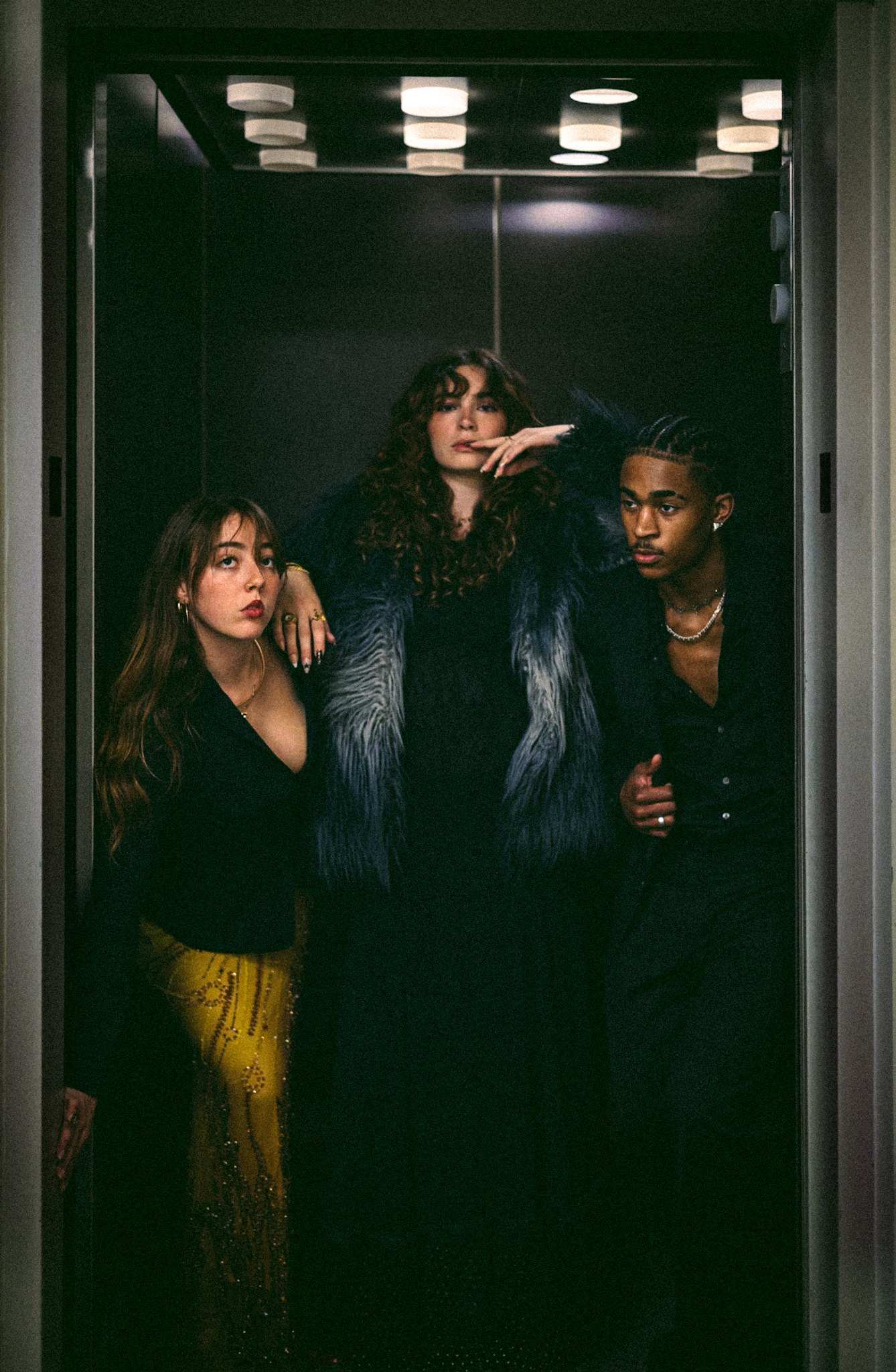 Three people stand close together inside an open elevator