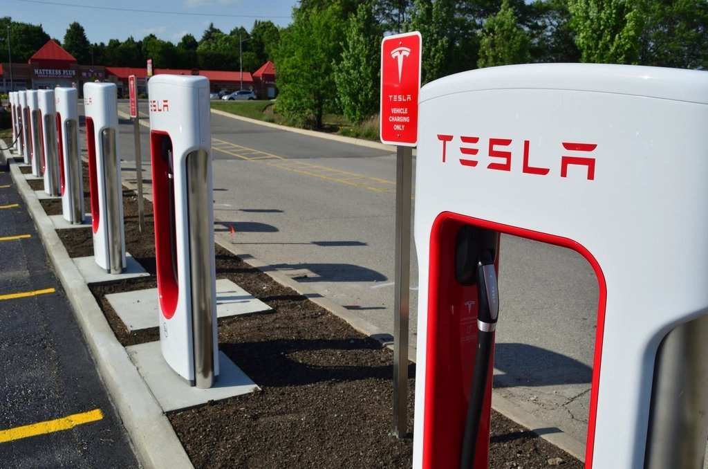 A row of white and red Tesla Supercharger stations beside a car park