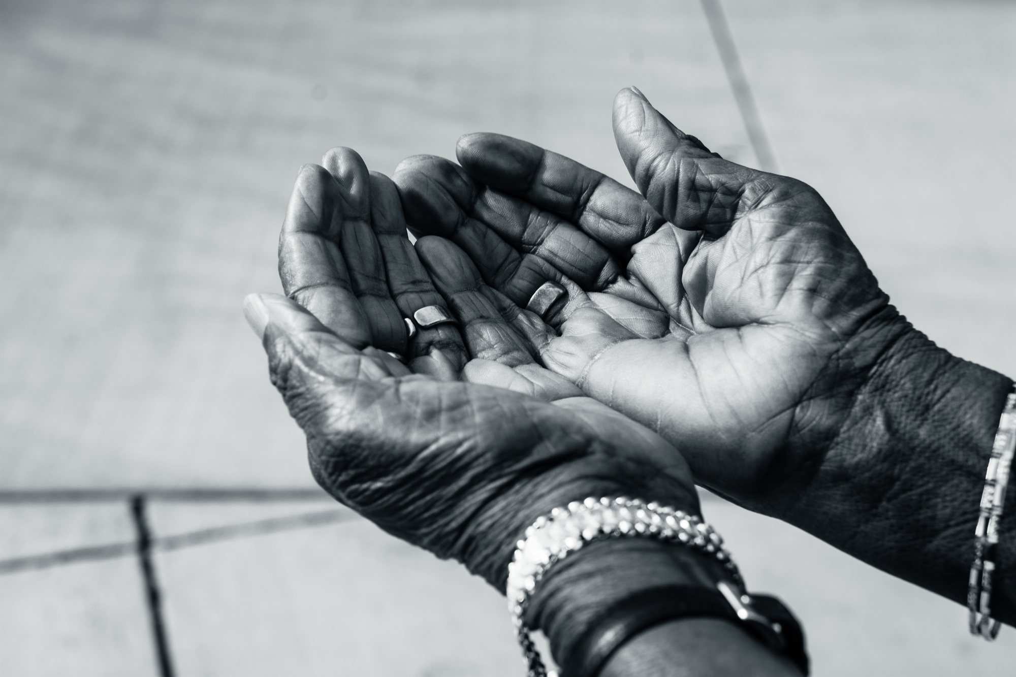 Black and white close-up of an older person's hands held open, with rings and bracelets