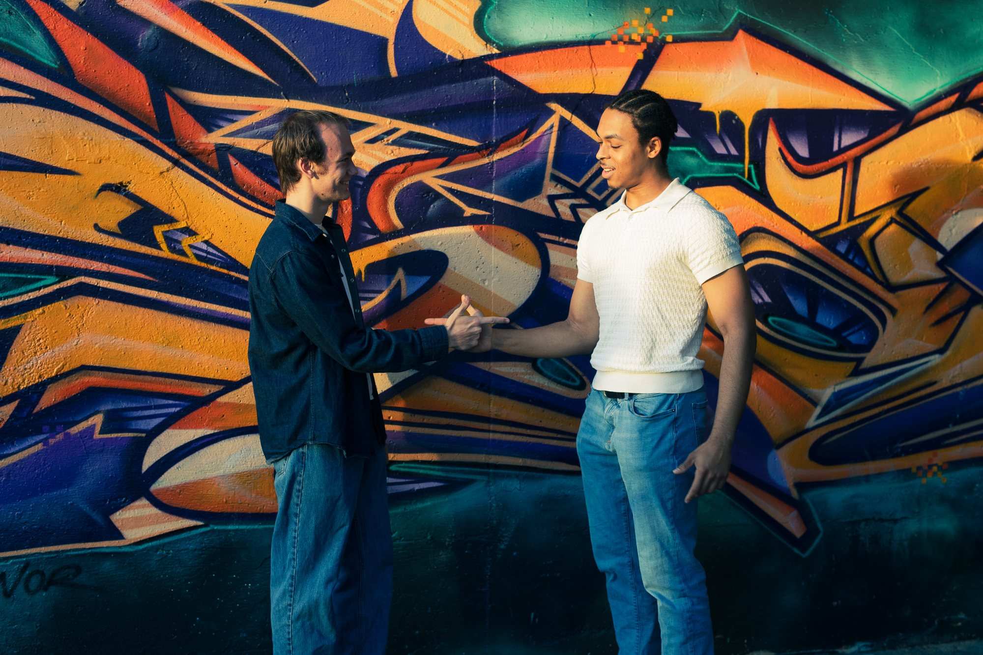 Two men shake hands in front of a colourful graffiti mural