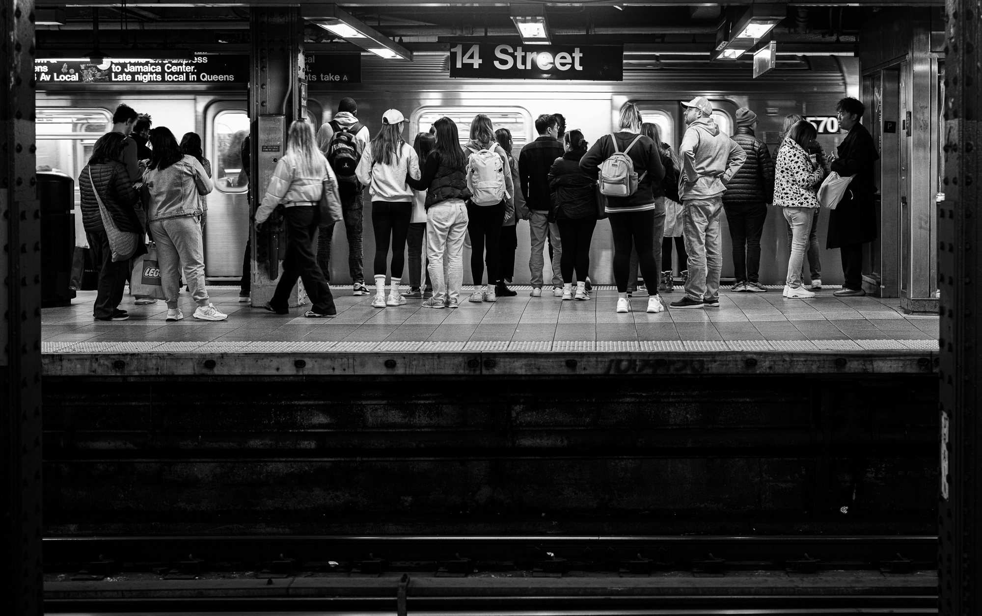 Black and white photo of people waiting on a subway platform at 14 Street